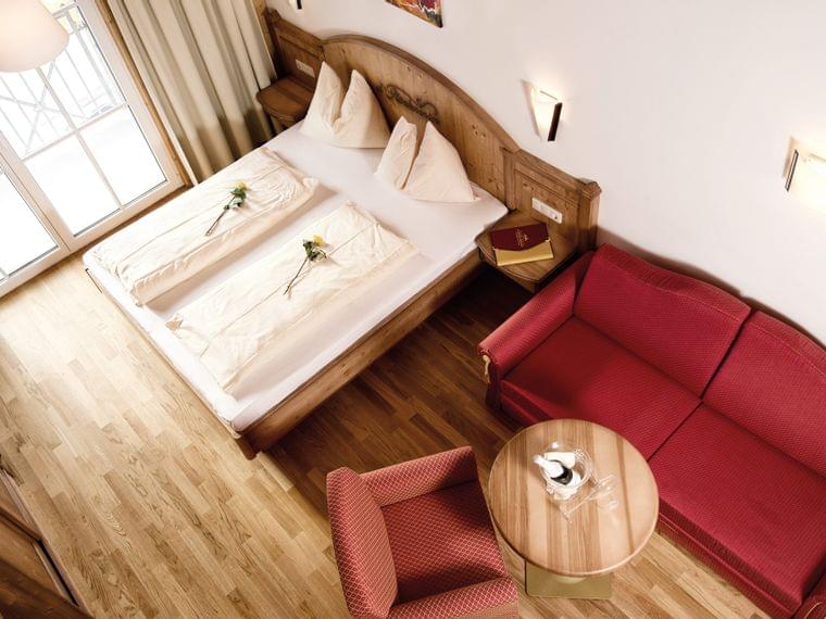 Rosenquarz Suite Gemütliches Hotelzimmer mit Doppelbett, rotem Sofa, Holzboden und Tageslicht